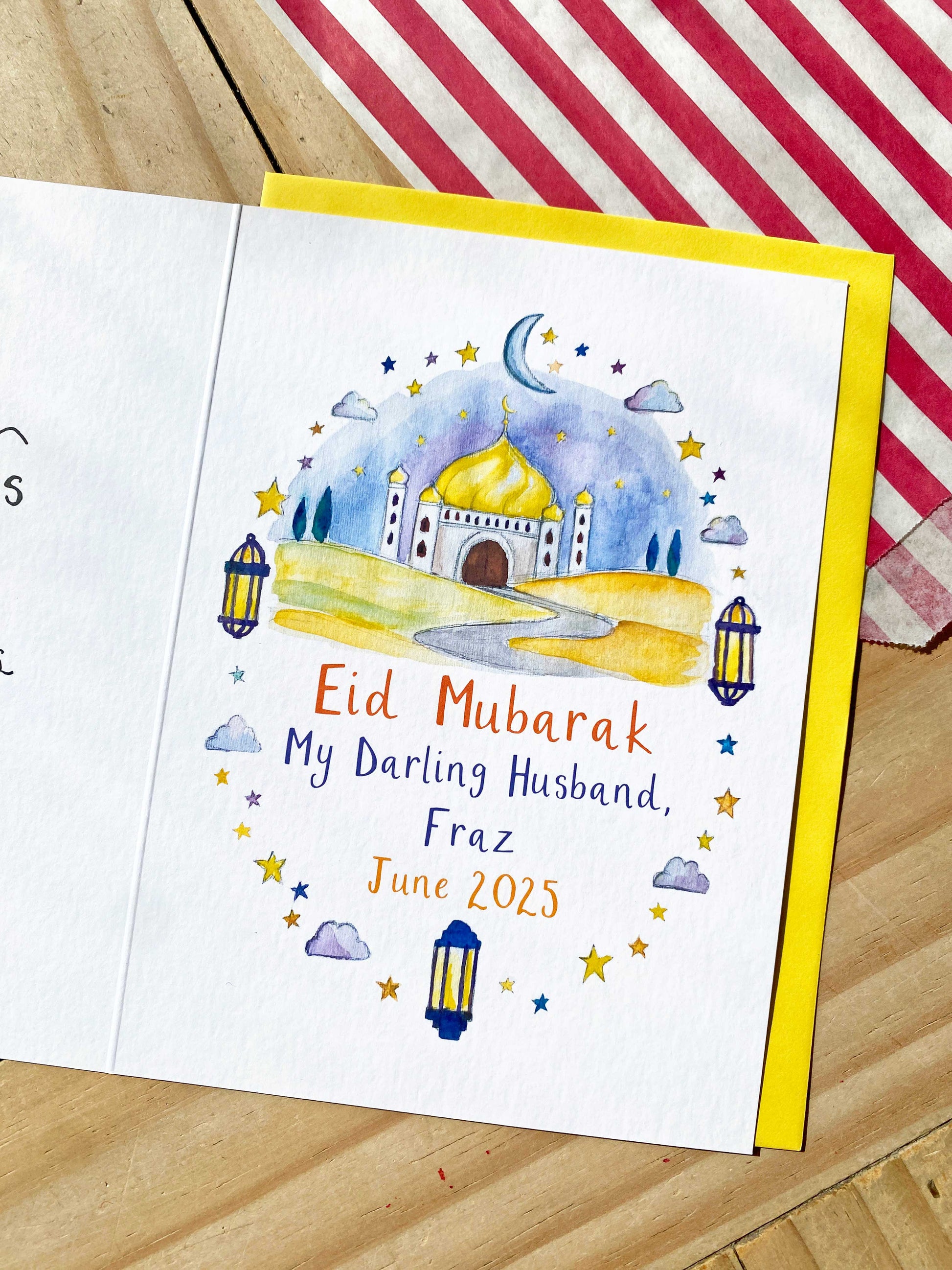 Eid Mubarak card with a mosque illustration on a wooden surface