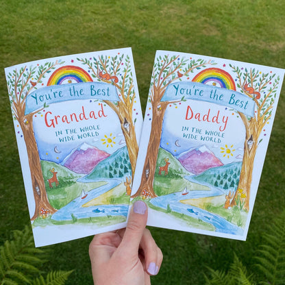 hand holding 2 cards that feature watercolour woodland scenes with mountains in the background. one card says 'you're the best grandad in the whole wide world' and the other  'you're the best daddyin the whole wide world'