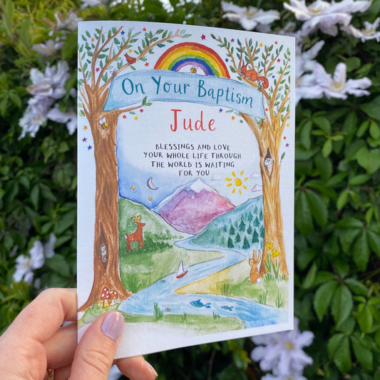 hand holding a watercolour card featuring woodland and mountain illustration and the text On your baptism' with personalised name below
