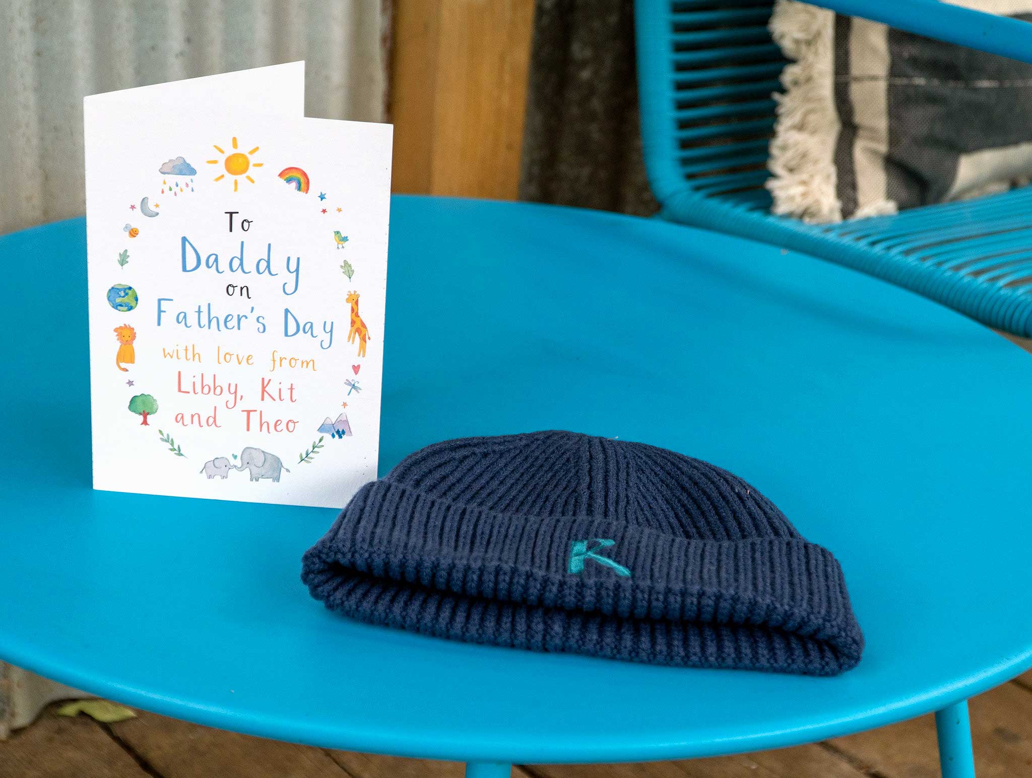 Navy knit beanie with embroidered logo next to a Father's Day card on a blue table.