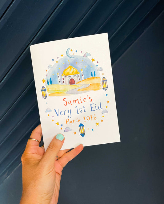 Hand holding a personalised card with the text 'Samie's Very 1st Eid' and watercolour design against a dark background