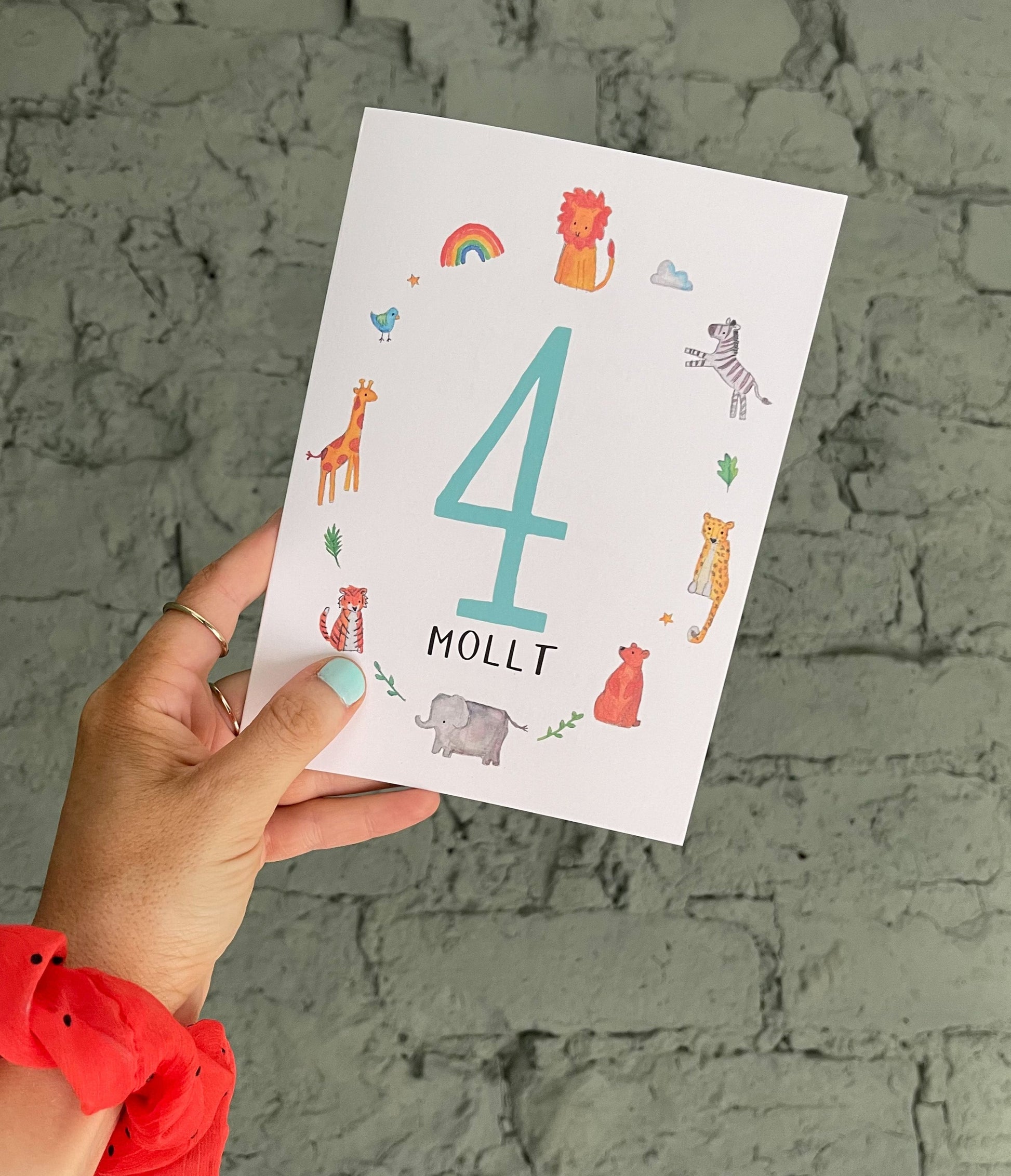 A hand holding a personalised birthday card with the number 4 and the name 'Molly' on it, featuring colorful animal illustrations around the number.