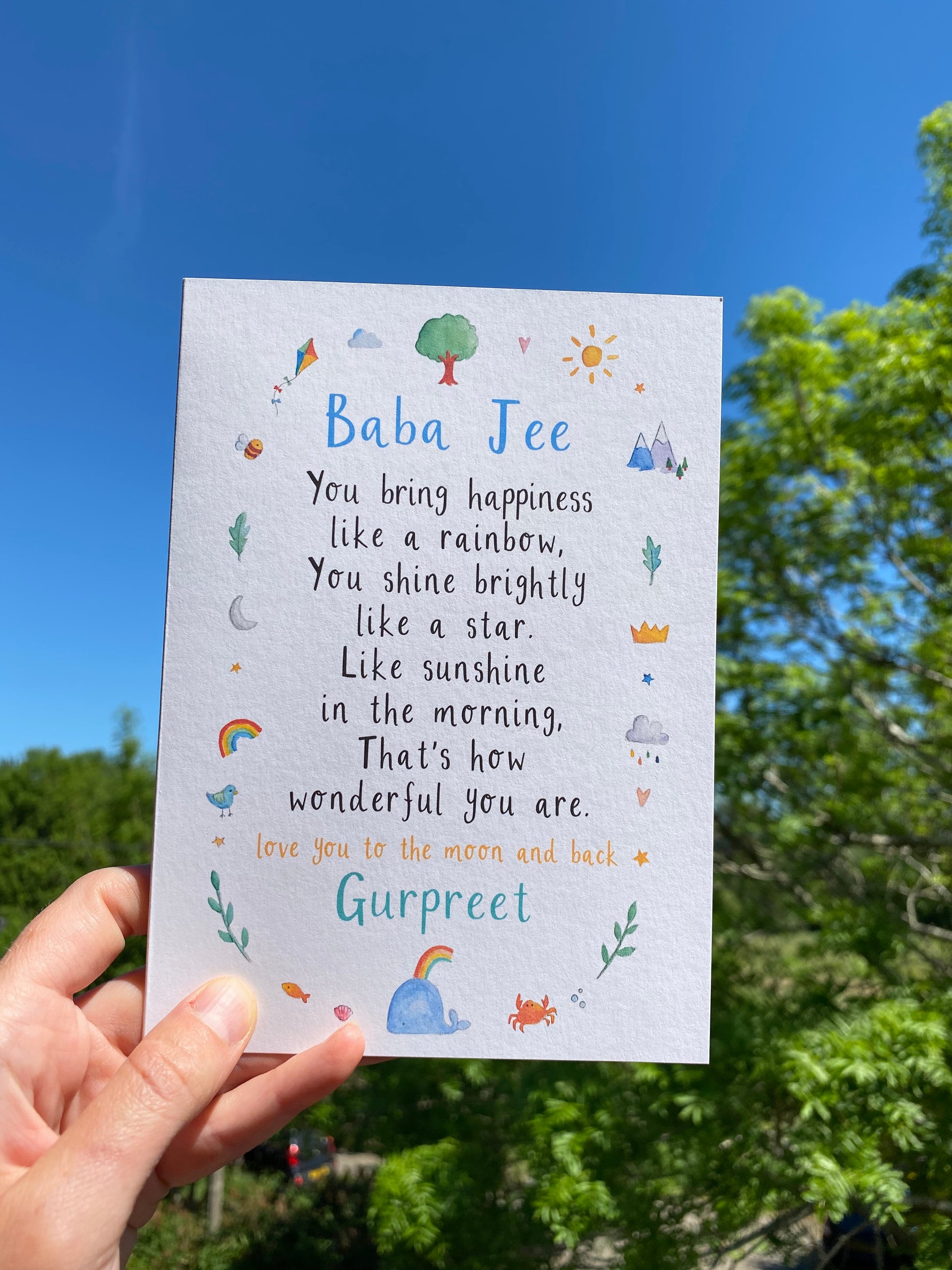 hand holding a white greetings card with the text 'baba jee' at the top, a poem underneath and watercolour illustrations surrounding it.