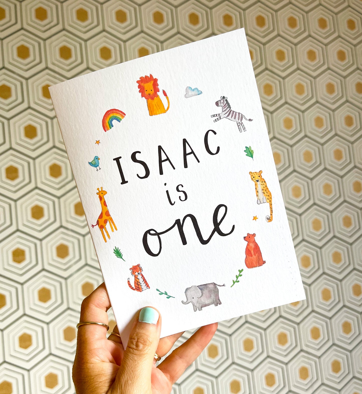 hand holding a white birthday card with watercolour animal illustrations and the text 'Isaac is one'