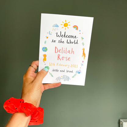 hand holding a white greetings card with watercolour animal illustrations and the text 'welcome to the world' with the child's personalised name