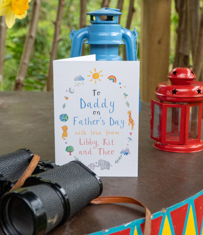 a greetings card with the text 'to daddy on Father's Day with love from libby, kit and theo' stands on a wooden table next to binoculars and a lantern