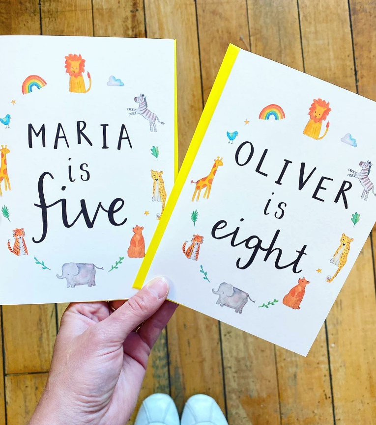 hand holding two custom birthday cards. one says 'maria is five' the other 'oliver is eight' surrounded by watercolour animal illustrations