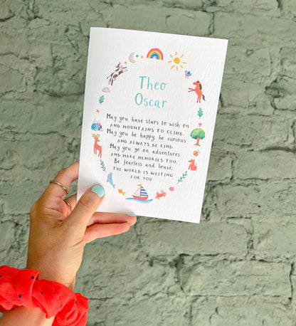 hand holding a white greetings card featuring colourful, watercolour illustrations surrounding a poem and the personalised name 'theo oscar' in front of a brick wall